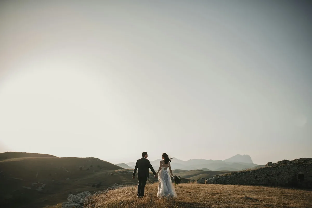 Bride and groom walking together on a grassy hillside at sunset
